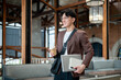 © bongkarn - Brown suit man with glasses walking while holding a coffee cup with notebook and laptop the in cafe.