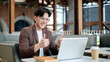 © bongkarn - Brown suit asian man with glasses is giving thumbs up to his laptop. Online meeting or presentation.