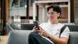 © bongkarn - Asian man wearing glasses in white t shirt is smiling as he looks at his phone while sitting in cafe