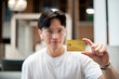 © bongkarn - Asian man wearing glasses in white t shirt holding or showing a yellow credit card. Card payment.