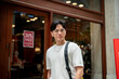 © bongkarn - Asian man wearing glasses in white tee looking into camera in front of a shop in shopping mall.