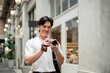 © bongkarn - Asian man with glasses in white tee is smiling while taking photos on camera in shopping mall or market.