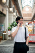 © bongkarn - Asian man with glasses in white tee walking hand in pocket while talking on phone in mall or market