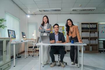 Poster - Three Asian businesspeople smiling and collaborating in a modern office, working together on laptops, taking notes, and engaging in lively discussions about ongoing projects