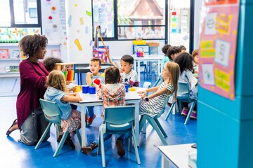 Poster - Diverse classroom with children and a teacher. Kids of various ethnicities learning together. Teacher guiding students in a colorful classroom setting. Teacher working with elementary school children.