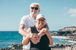 © luciano - Joyful senior couple enjoys a beautiful day by the ocean, hugging each other with smiles. Background of rocky coastal landscape, a perfect scene of love, companionship and happiness in retirement