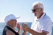 © luciano - Smiling senior pensioner couple hands in hands face the sea enjoying freedom and vacation, Background of blue ocean and sky, a perfect scene of love, companionship and happiness in retirement