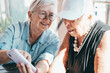 © luciano - Two elderly women joyfully sharing a moment looking at a smartphone together. Their expressions convey happiness, friendship, positivity and companionship, staying connected in the digital age