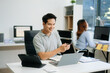 © Nuttapong punna - Confident business expert attractive smiling young man typing laptop and holding digital tablet on desk