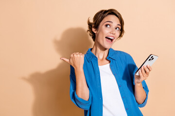 Poster - Photo of young businesswoman pointing finger mockup when holding smartphone analyzing prices website isolated on beige color background