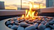 © yong - An outdoor fire pit filled with pebbles, surrounded by folded towels, with a beautiful sunset in the background.