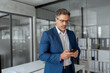 © Stock 4 You - Focused Indian mature businessman in suit and eyeglasses holding smartphone standing in office, working on device. Middle eastern arab or latin senior business manager man ceo using cell phone mobile