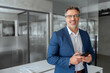 © Stock 4 You - Smiling Indian mature businessman in suit holding smartphone standing in office, working on device. Executive professional ceo senior business manager man using cell phone mobile, looking at camera