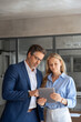 © Stock 4 You - Team of mature senior leader man in suit and young employee woman discussing project on tablet standing in office. Two colleagues of professional business people looking at screen device. Vertical