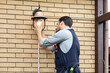 © Vitaliy - Young handsome electrician standing on ladder and change the light bulb in house facade on the backyard