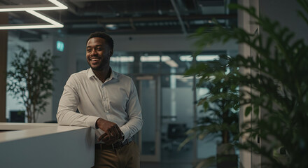 Poster - Smiling black businessman leaning on desk in modern office lobby