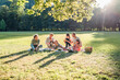 © Soloviova Liudmyla - Big family sitting on picnic blanket under linden trees in a city park on sunny day. They are chatting and eating boiled corn and watermelon. Family values and outdoor activities concept.