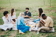 © qunica.com - A diverse group of friends sits on a blanket having a picnic. They enjoy food and conversation in a lush park setting, embodying relaxation and connection.