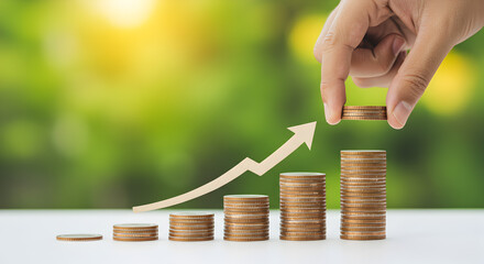 Poster - Hand Adding Gold Coins to Stacks Displaying Business Growth Against Green Blurred Background
