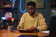 © DragonImages - African American man sitting at table and reading content plan before podcast in studio