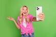© deagreez - Happy young woman in a pink shirt taking a cheerful selfie against a vibrant green background