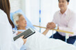 © DG PhotoStock - Elderly Asian woman resting in a hospital room with her son visiting.