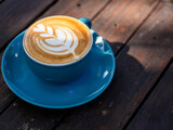 A cup of cappuccino coffee, with a blue cup placed on a black wooden table. Beautiful latte art with leaf shape.