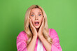 © deagreez - Portrait of a surprised young woman holding her face with wide eyes against a green background wearing stylish pink shirt.