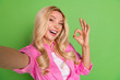 © deagreez - Young blonde woman in a pink shirt making an okay gesture with a cheerful smile against a vivid green background