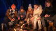 © kinomaster - Friends sitting around a campfire in the woods on a winter evening