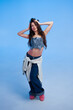 © callisto - Young woman poses confidently in stylish outfit against blue backdrop