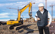 © Grispb - Construction manager with tablet inspects building site with excavator and cranes in background, supervising progress and heavy equipment work – Construction. Machinery repair.