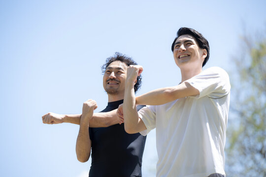 青空の中二人でスポーツの準備運動してストレッチする男性2人