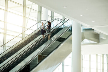 Poster - Business, women or travel on escalator in office for meeting commute, work arrival or career discussion. Professional, people or talking on moving staircase for corporate journey or seminar departure