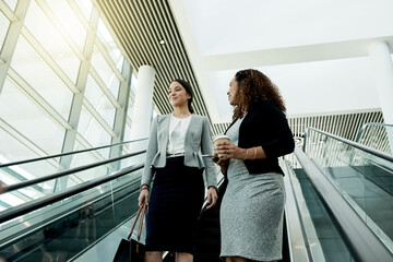 Poster - Office, escalator and business women in morning in lobby for meeting, discussion and conversation. Professional workers, corporate and people at conference, convention and seminar in modern building