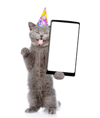Aufkleber - Happy cat with tongiye out wearing party cap standing on hind legs and shows big smartphone with blank screen. Empty space for text. isolated on white background