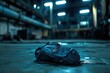 © hkjdesign - A dark blue backpack sits alone on a wet, industrial floor, possibly lost or abandoned.