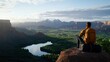 © Vangly - Man enjoying a serene mountain view at sunrise with a peaceful lake below.