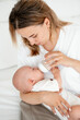 © Any Grant - mom feeds the baby with a bottle of milk or formula, feeding the baby in her arms, a young mother feeds the newborn baby at home on the bed