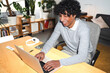 © Studio Marmellata - An Arab young man is working on his laptop at home. He is smiling and seems to be enjoying his work in a bright, plant-filled space.