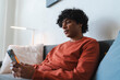 © Studio Marmellata - An Arab young man relaxes on the sofa at home. He is using his smartphone to browse the internet or connect with friends.