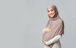 © Prostock-studio - Pregnancy And Islam Concept. Beautiful pregnant muslim woman in hijab touching her belly, posing over gray background with free space