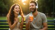 © Thiago - Couple laughing and holding smoothies while sitting on a park bench in the sunshine outdoors together