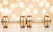 © SutikawatiVibes - Golden dumbbells placed on surface with bokeh background, fitness equipment for weight training and exercise