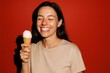 © Volha - Young woman smiling joyfully holding ice cream against red background