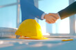 © mcjanuald - Construction agreement handshake with yellow helmet and architectural plans