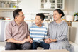 © winnievinzence - Happy Asian grandson and grandparents relax sitting on couch in the living room looking at camera. Family generation love bonding, people smiling and laughing together at home