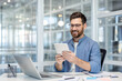 © Liubomir - A man smiles while using a tablet device at his modern office desk. The professional looks engaged and is surrounded by office equipment.
