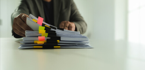 Poster - Stacks of paper files and checking document businessman checks financial documents on his laptop, managing corporate reports and legal paperwork at his office desk.