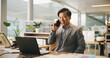 © peopleimages.com - Business, phone call and Asian man with laptop, smile and communication with financial advice. Pc, employee and accountant in office, cellphone or conversation with tax review, talking or feedback